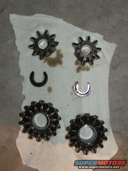 Four metal spider gears and two c-clips laid out on a white cloth
