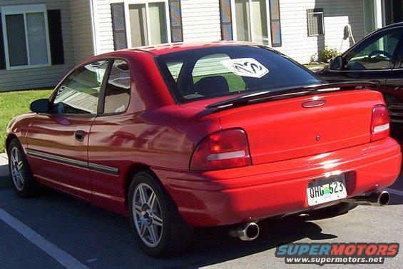 Red coupe with a spoiler and dual exhaust pipes, parked next to a dark SUV