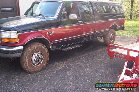 Side view of a red and black Ford F-250 pickup truck with a camper shell