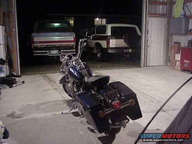 Dark blue Harley-Davidson motorcycle parked in a garage with two trucks in the background