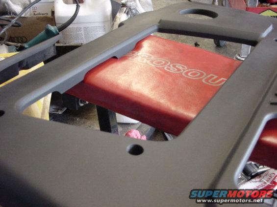 Gray plastic car dashboard trim piece with red seat visible underneath