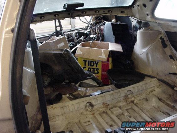 Car interior stripped down, wires exposed, with a box of Tidy Cats litter and other parts