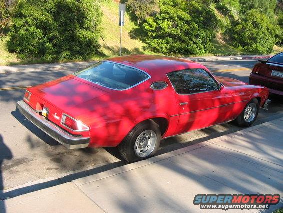 Red 1970s coupe parked curbside, another car behind it
