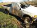 1979 Ford F-150 - This damaged white pickup truck appears stuck in a muddy field, with a tarp obscuring the driver's side door and window.