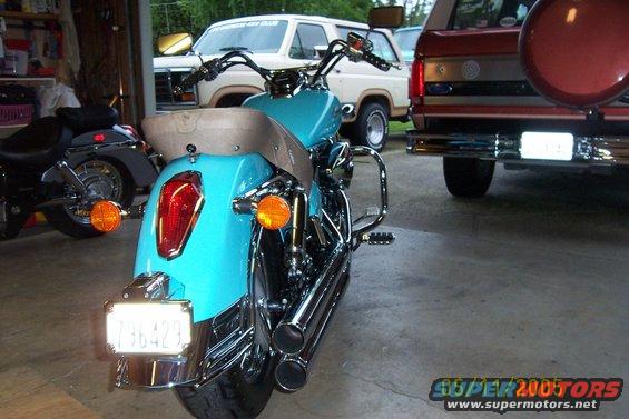 Rear view of a turquoise motorcycle with chrome pipes and a license plate reading 736429