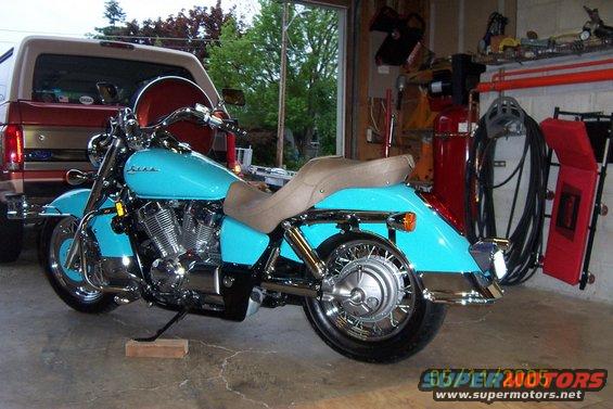 Turquoise motorcycle with a tan seat parked in a garage next to a red SUV