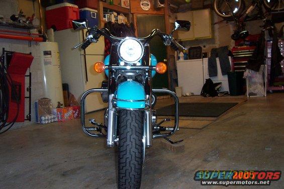 Turquoise motorcycle with chrome crash bars and a round headlight, parked in a garage