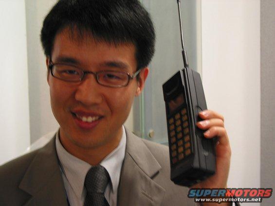 Man in suit and tie holding a large, early mobile phone with an antenna