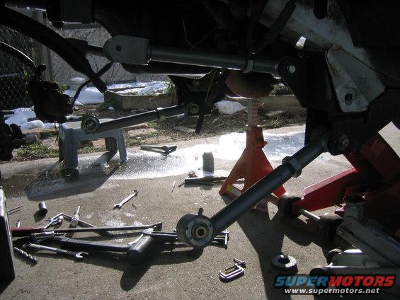 Suspension components and tools on the ground, with "SUPERMOTORS.NET" visible