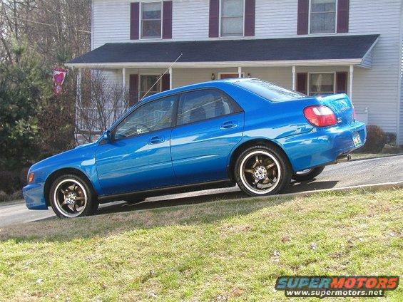 Blue 2002 Subaru Impreza sedan with aftermarket wheels parked on grass