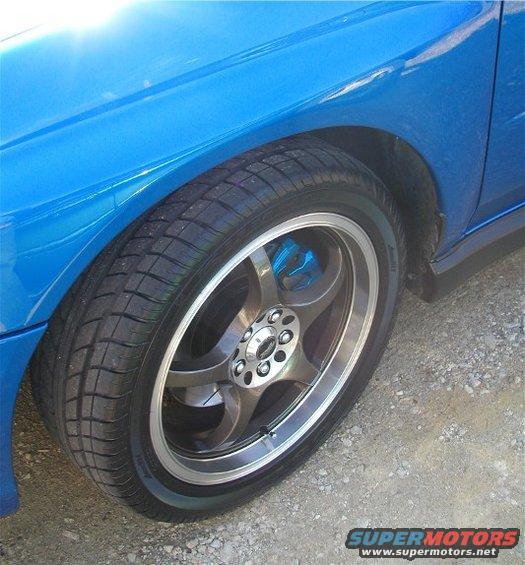 Close-up of a blue 2002 Subaru Impreza WRX wheel and fender. It has aftermarket rims and blue brake calipers