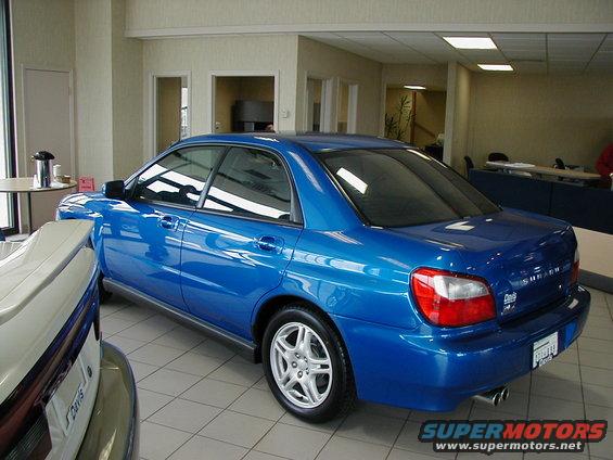 Blue 2002 Subaru Impreza sedan parked indoors, rear 3/4 view. Visible badge on trunk reads 'SUBARU'