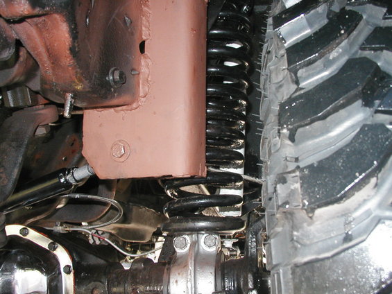 Close-up of a vehicle's suspension with a large coil spring and a knobby tire. The frame is painted brown