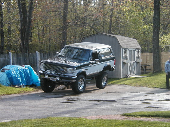 Two-tone dark green and silver lifted Ford Bronco with aftermarket lights on front bumper