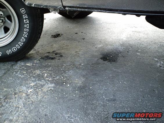 Dark vehicle side panel and tire with "DESTINATION" text, on asphalt with oil stains