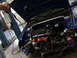 1998 Volkswagen Jetta - The engine bay of a blue car is exposed with the hood open, revealing complex wiring and mechanical parts.