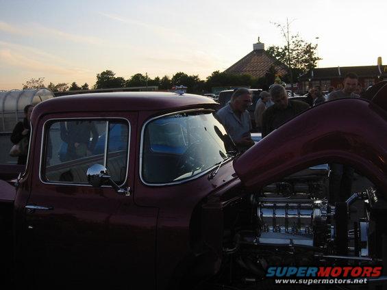 Maroon pickup truck with hood open showing a chrome engine, people gathered around