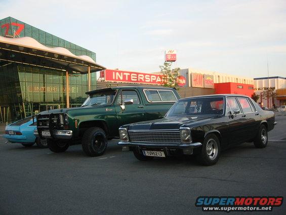 Black sedan parked in front of a building with a green SUV and blue car