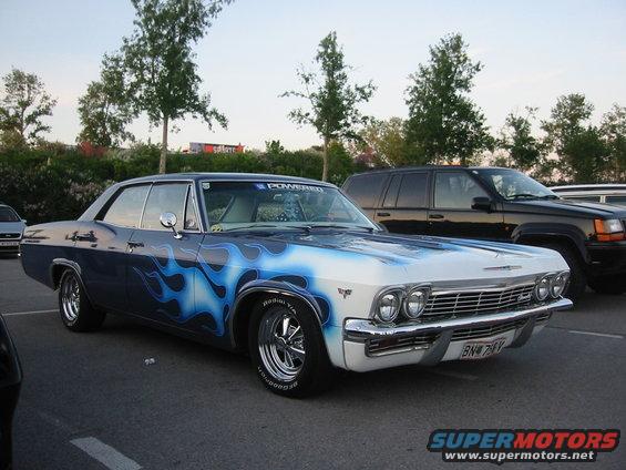Customized 1965 Chevrolet Impala with blue flames painted on the hood and sides, parked next to a black SUV