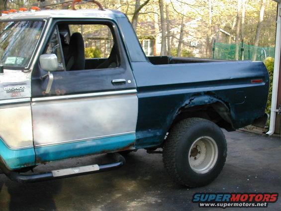 Side view of a 1979 Ford Bronco with primer and dark teal paint, showing rust repair