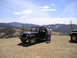 1989 Ford Bronco - Two people stand by a black Jeep Wrangler on a dirt road with a mountainous landscape behind them.