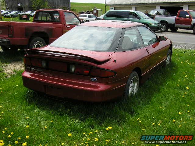 red coupe parked in grass, red pickup truck behind it