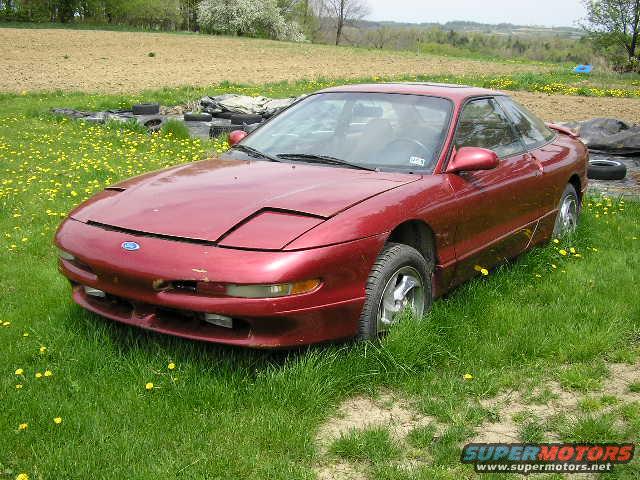Red coupe with pop-up headlights parked in a grassy field