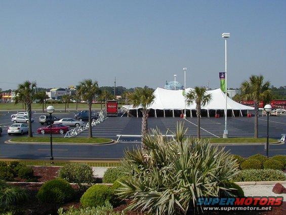 Red sports car parked in a lot with a large tent in the background