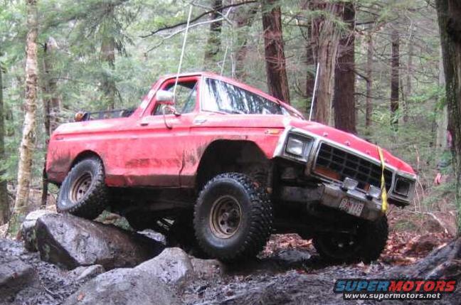 red SUV with large tires driving over rocks in a forest
