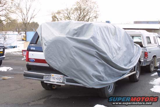 Rear of a Ford Bronco covered by a gray car cover, license plate YKE-6125 visible