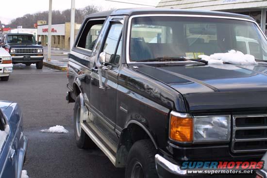 Black 1989 Ford Bronco parked outside, with a white truck in the background