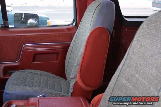Car interior with red door panel and grey patterned seats. A side mirror is visible through the window