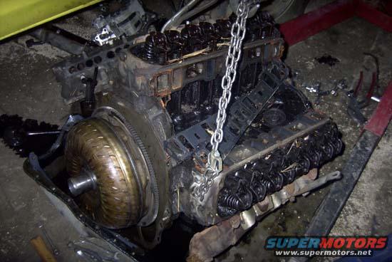 Engine with torque converter hanging from a chain, covered in grime