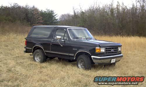 Black Ford Bronco parked in a grassy field with trees in the background