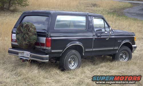 1989 Ford Bronco parked in a grassy field, spare tire mounted on rear door