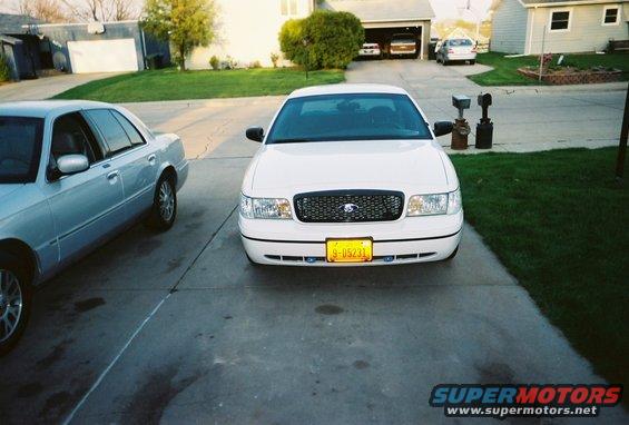 White 2000 Ford Crown Victoria parked in driveway next to a silver car. Garage in background