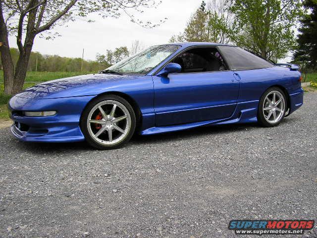 Blue coupe with aftermarket wheels parked on gravel