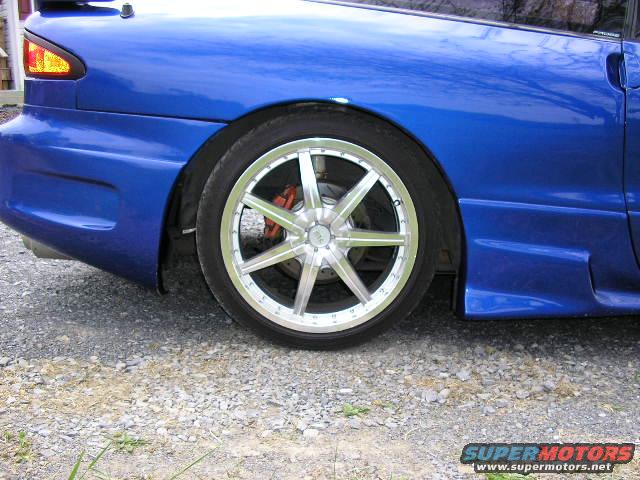 1994 Ford Probe rear wheel with custom silver rims and red brake caliper. Blue paint on fender and bumper