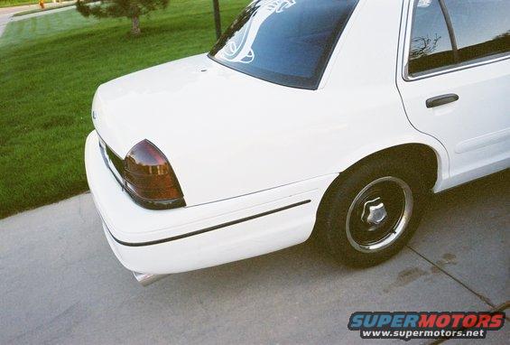 White sedan's rear quarter panel and tail light. Chrome exhaust tip visible