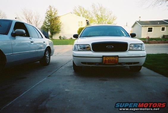 White 2000 Ford Crown Victoria parked on driveway, front view. Another silver sedan is to the left