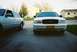 2000 Ford Crown Victoria - Two sedans are parked in a driveway, one white Ford Crown Victoria and a silver car.