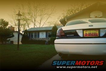 Rear of a white sedan parked in a driveway, house and yard in background