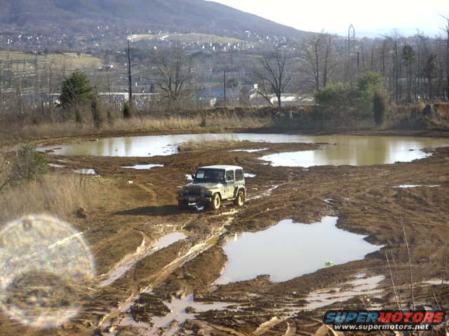 Green Jeep Wrangler stuck in mud, front-right tire submerged in water, side view