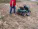 2003 Ford Ranger - A person is pulling a green riding lawn mower with a chain across a dry, grassy field.