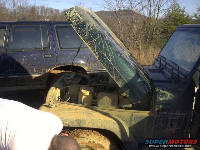 Jeep Wrangler engine bay with hood open, blue SUV behind