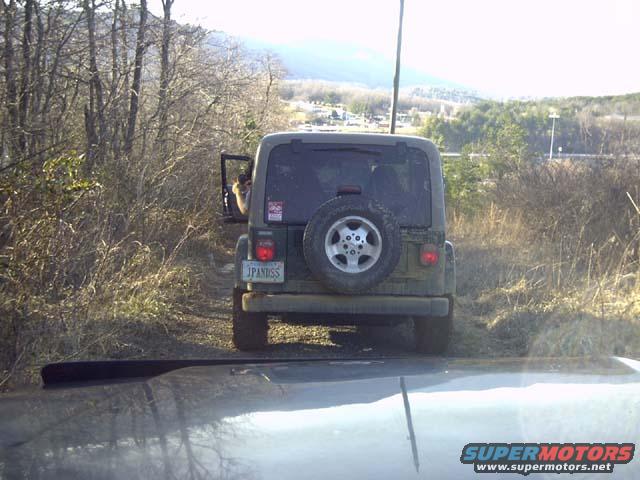Green Jeep Wrangler with spare tire on rear door, parked on dirt road