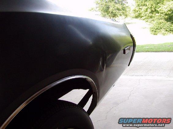 rear quarter panel of a dark-colored car, showing a dent and chrome trim around the wheel well