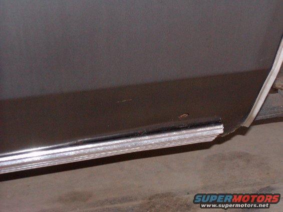 Close-up of a dark-colored vehicle's lower body panel with a chrome trim piece. Some rust is visible