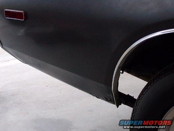 Close-up of a dark colored car's rear quarter panel, showing the taillight and wheel well
