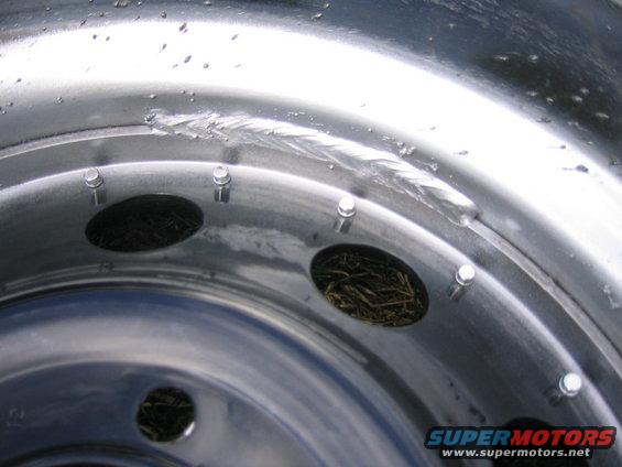 Close-up of a damaged metal wheel rim with visible scratches and debris inside the bolt holes